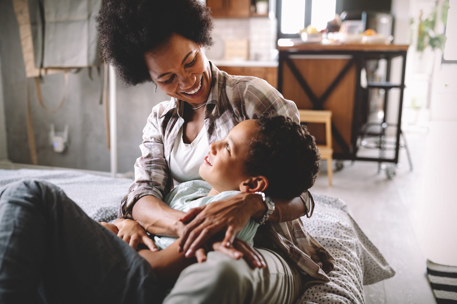 Happy african mother playing, having fun, hugging with her son at home